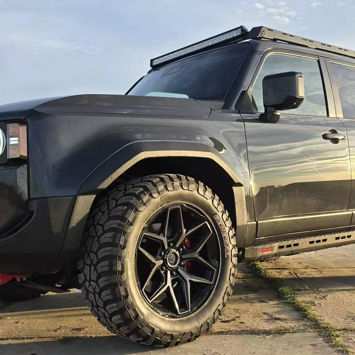Full side view of a black Land Cruiser 2024 (LC1958) showing the wide, protective wheel arches / fender flares and aftermarket off-road wheels.