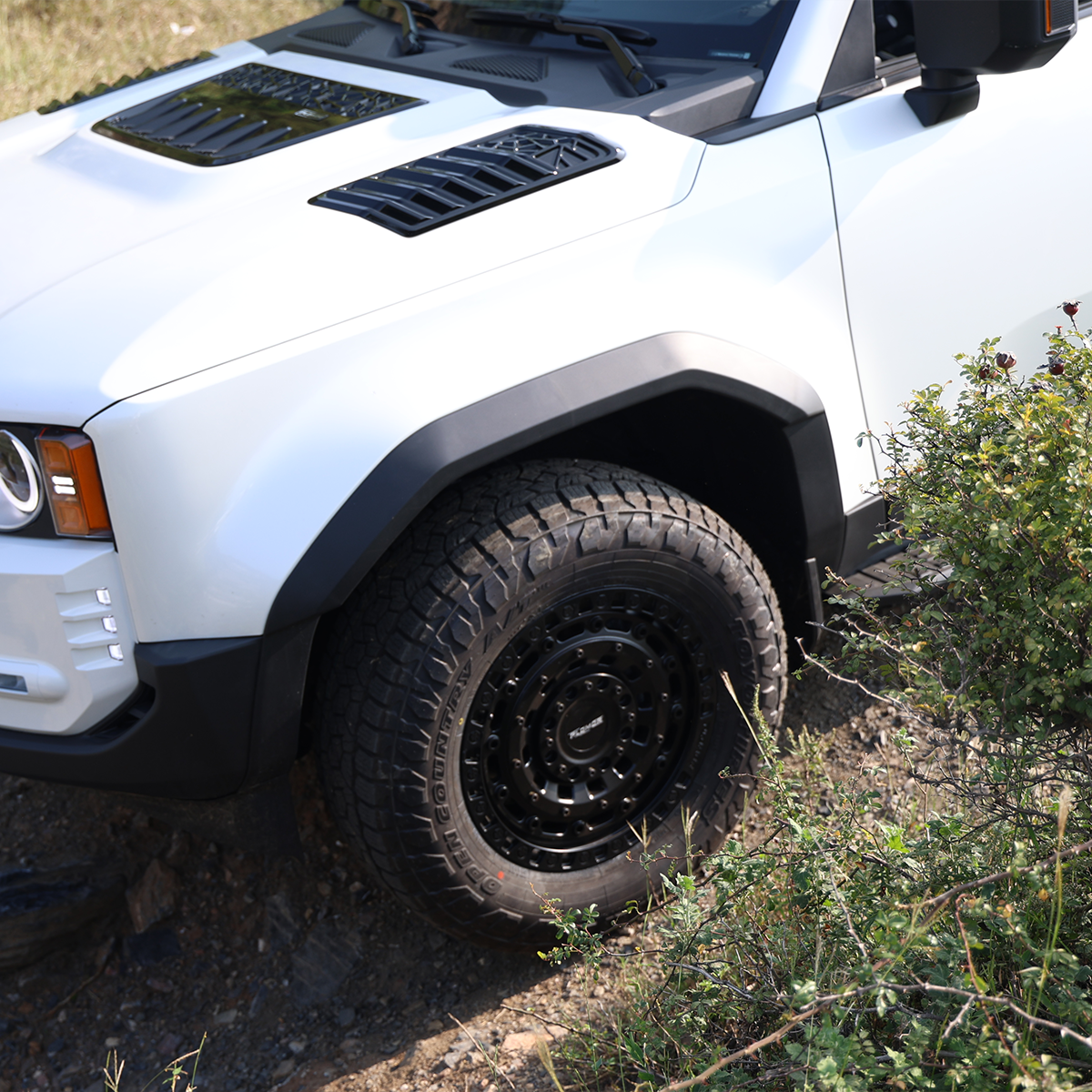 Close-up shot of a white Land Cruiser (LC1958) on an off-road trail, highlighting the black textured fender flares (wheel arches) and off-road tires.