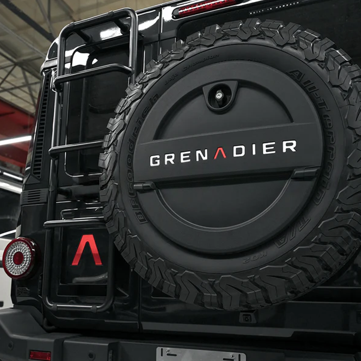 Red “A” logo decal on hood of a 2023+ INEOS Grenadier, emphasizing sporty front view on rugged terrain.