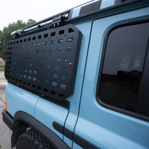 PLOMOR side window armor panel for the INEOS Grenadier, featuring a MOLLE-style grid, powder-coated steel construction, and a custom-fit bolt-on design for added protection and modular gear mounting.