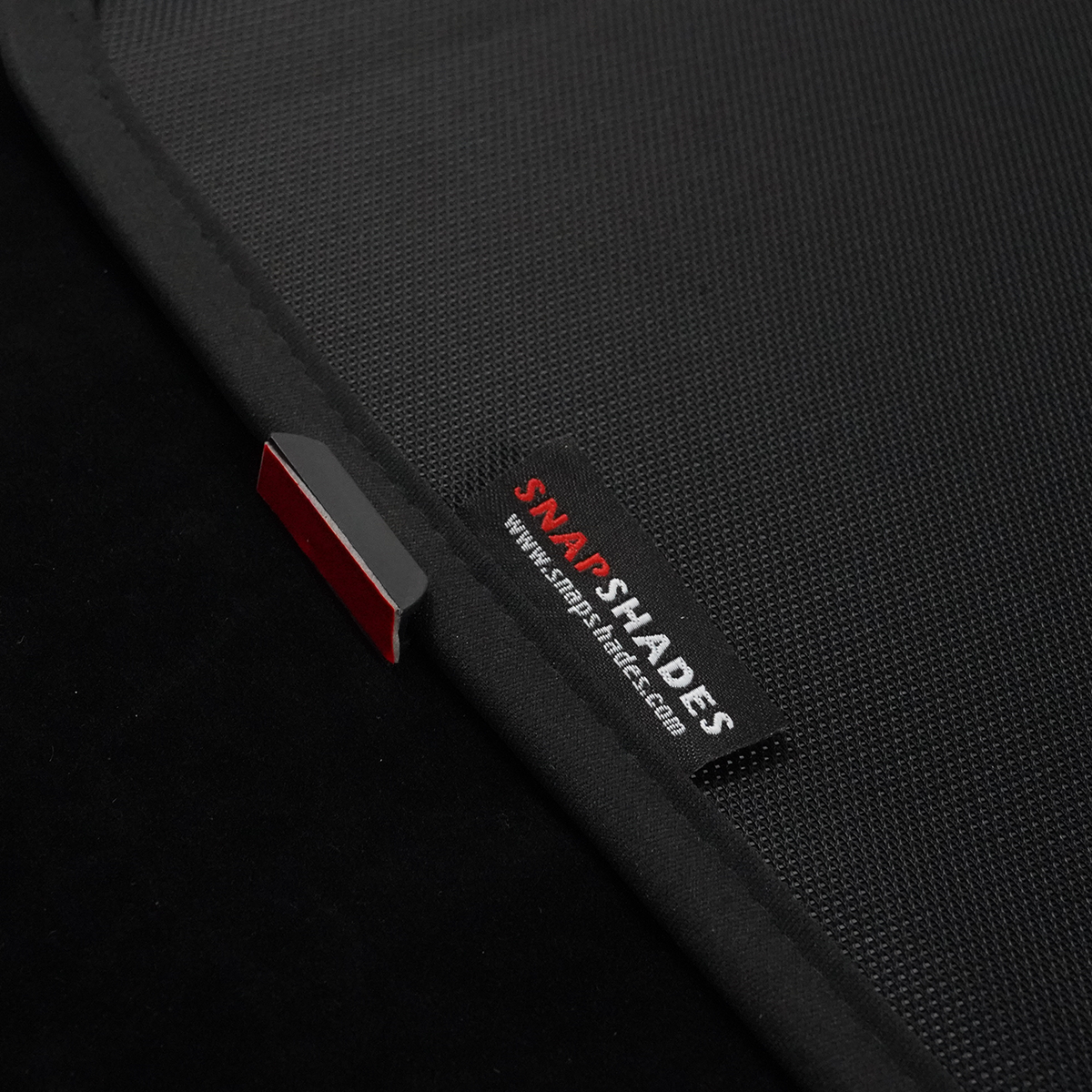 Close-up of skylight sunshade edge showing magnetic clip with 3M tape and woven label on mesh fabric.