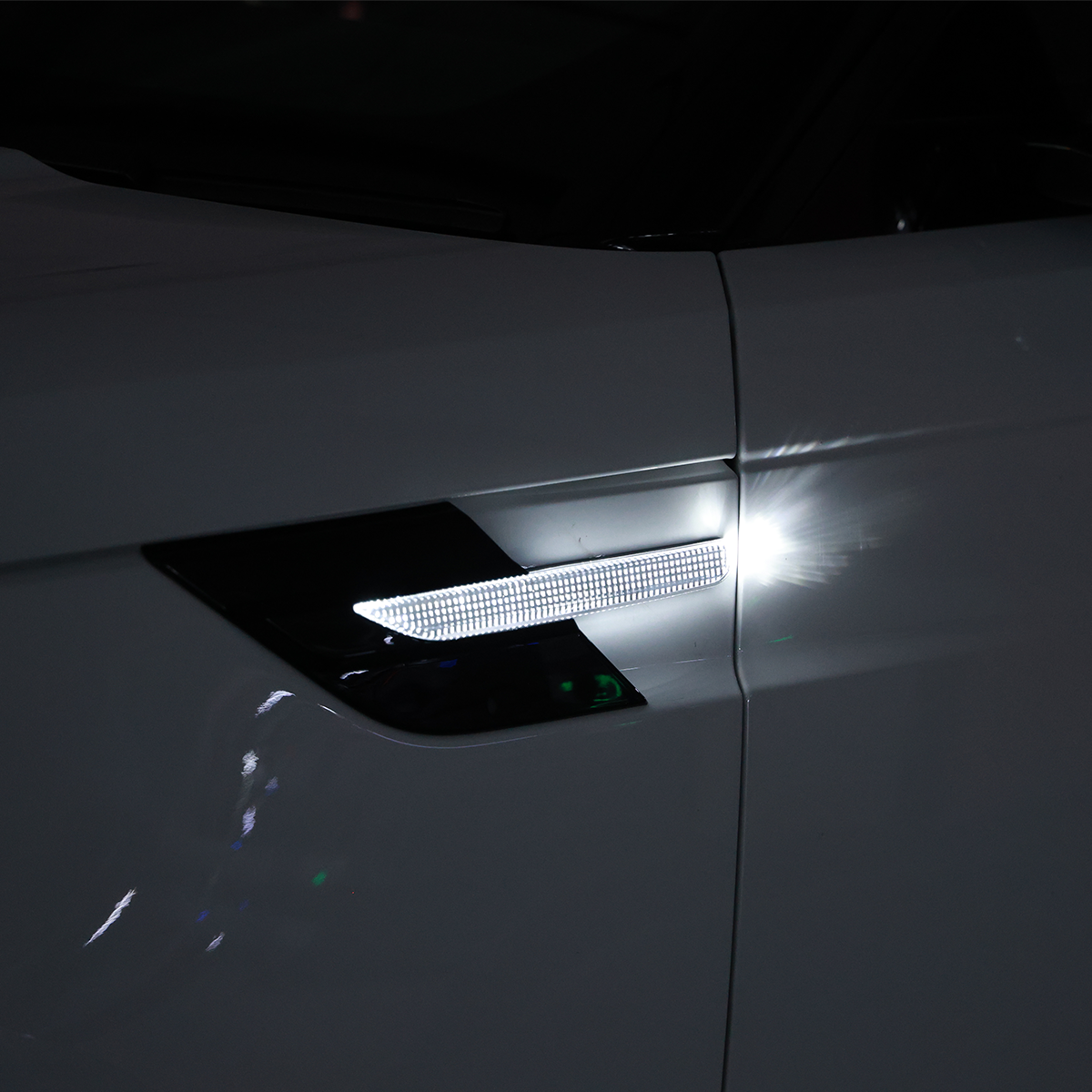 Night shot of a Range Rover fender side indicator/turn-signal trim in gloss black with the white light illuminated.