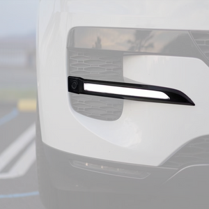 Close-up installed view of a gloss-black side LED light strip on a Range Rover front bumper, illuminated in daylight.