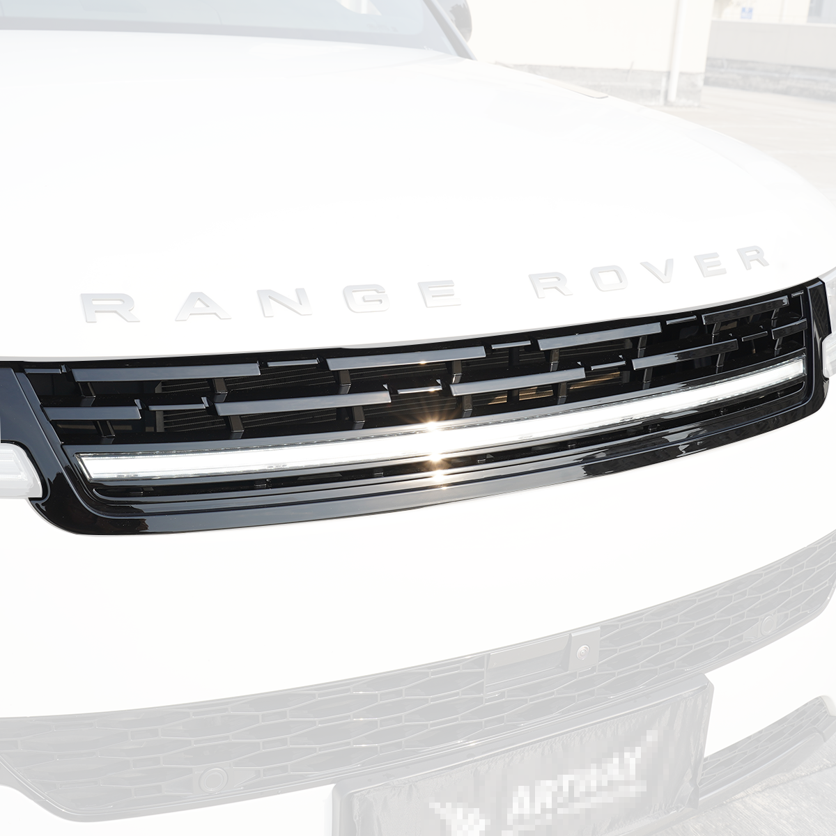 Close-up of a Range Rover front grille with an integrated LED light bar in gloss black finish, daytime shot.